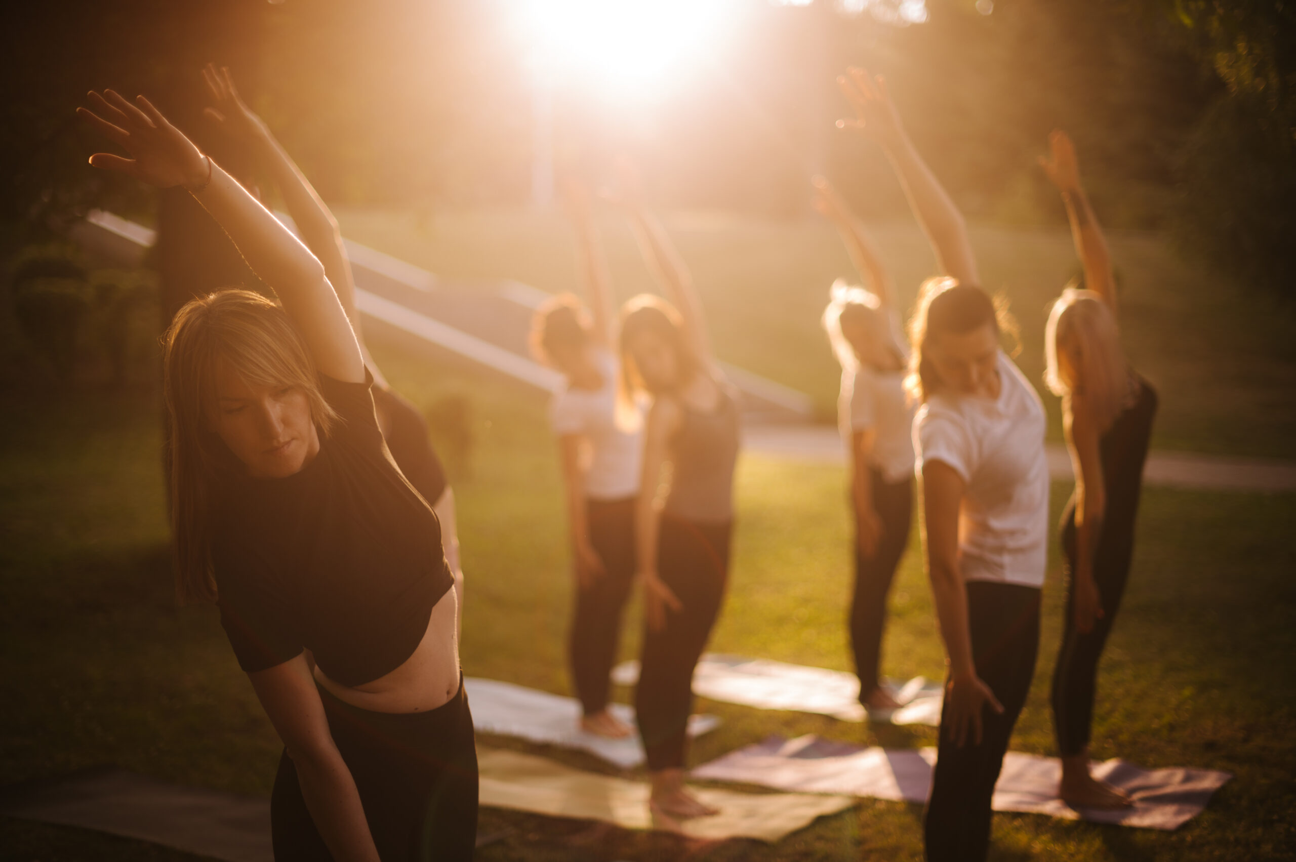 Group of women do yoga in city park on summer sunny sunrise or sunset