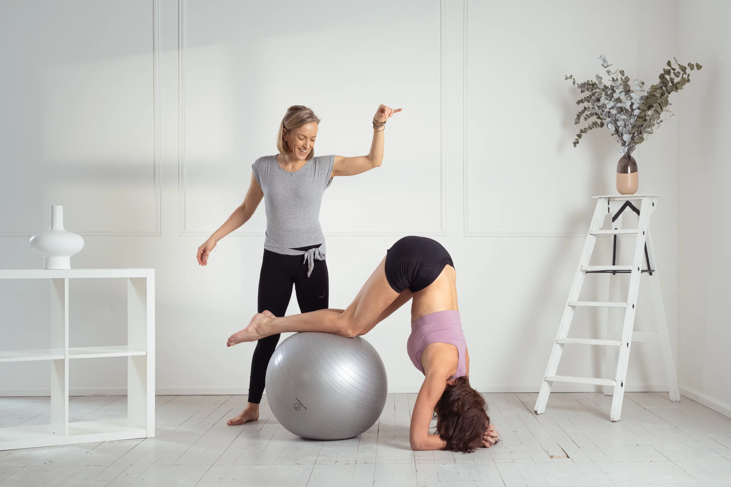 Marina, professeure de la méthode Mov'Art®, accompagne une élève lors d'un exercice de gainage inversé sur ballon de Pilates. Ce moment d'échange en studio illustre la précision pédagogique et la bienveillance nécessaires pour progresser en toute sécurité.